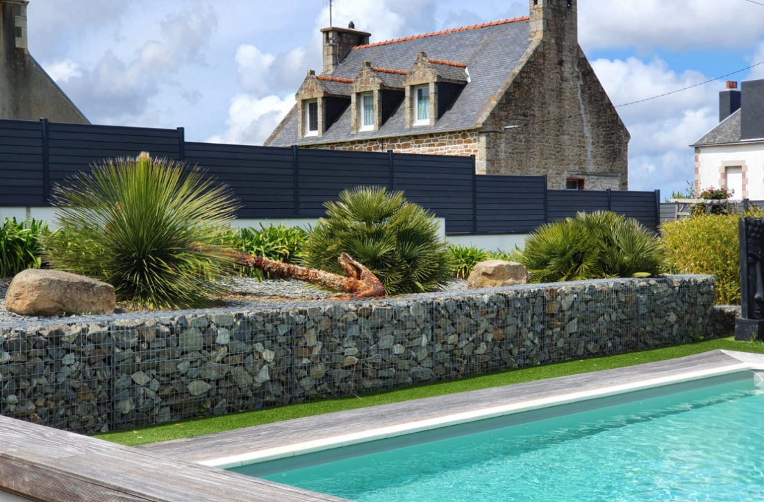 Ext&eacute;rieur avec cl&ocirc;ture gabion et plantes tropicales 